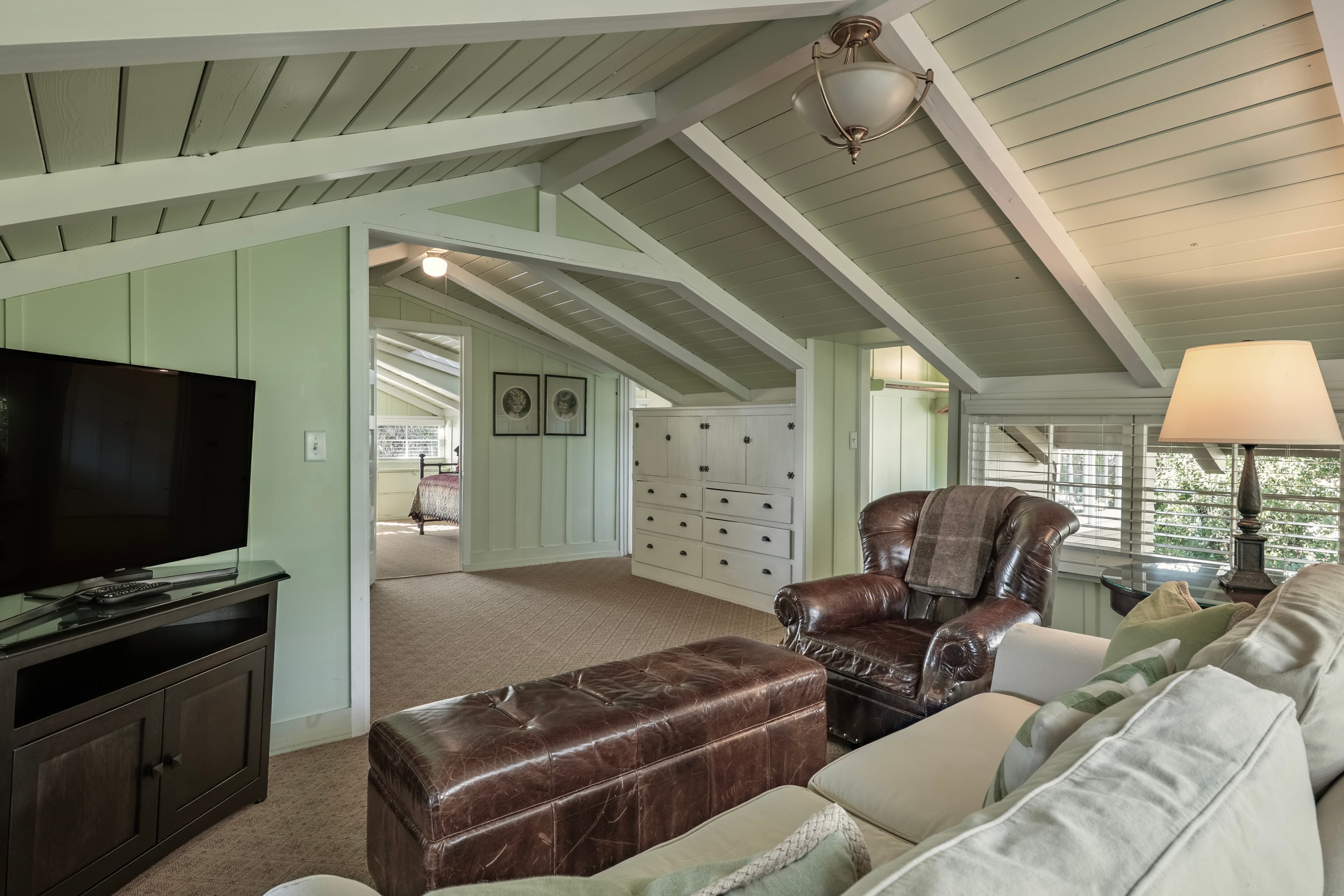Bright, airy attic living space featuring a leather chair, ottoman, and TV against green walls.