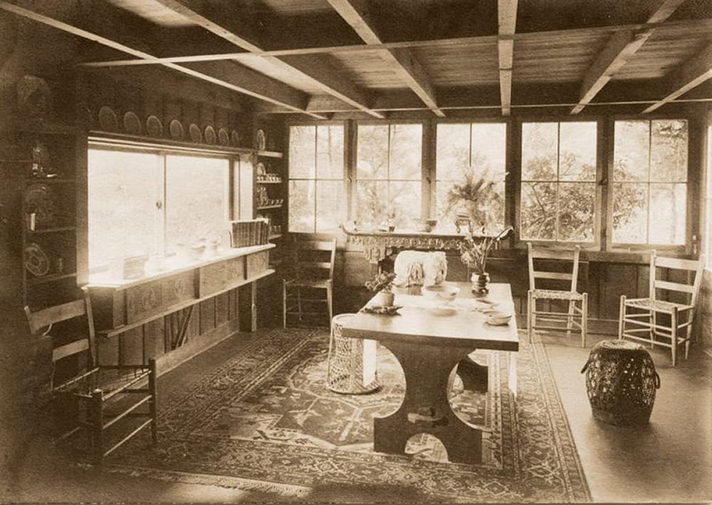 A vintage interior of a cozy room featuring a table, chairs, and large windows.