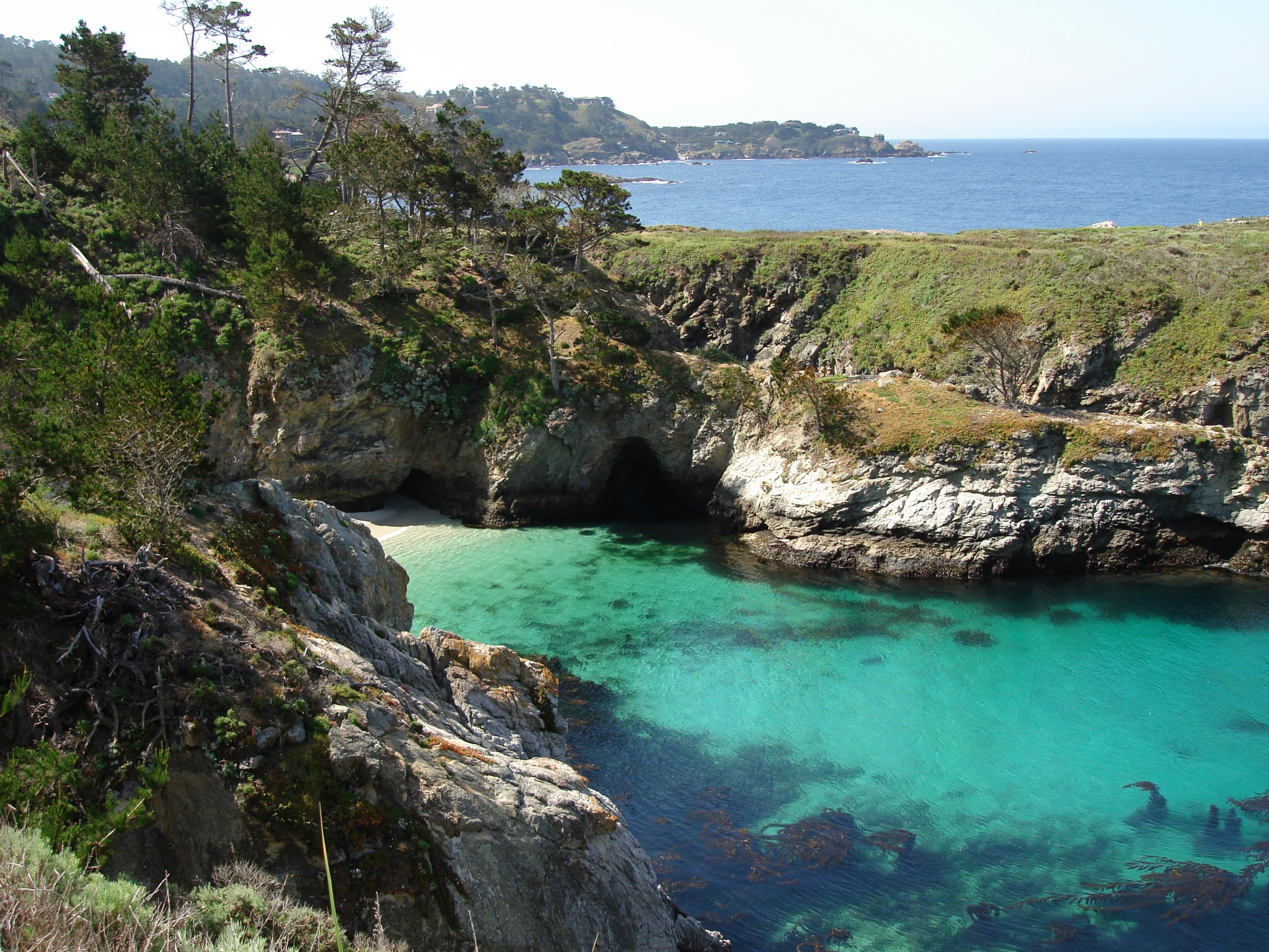 A scenic coastal view featuring turquoise waters, rocky cliffs, and lush greenery.