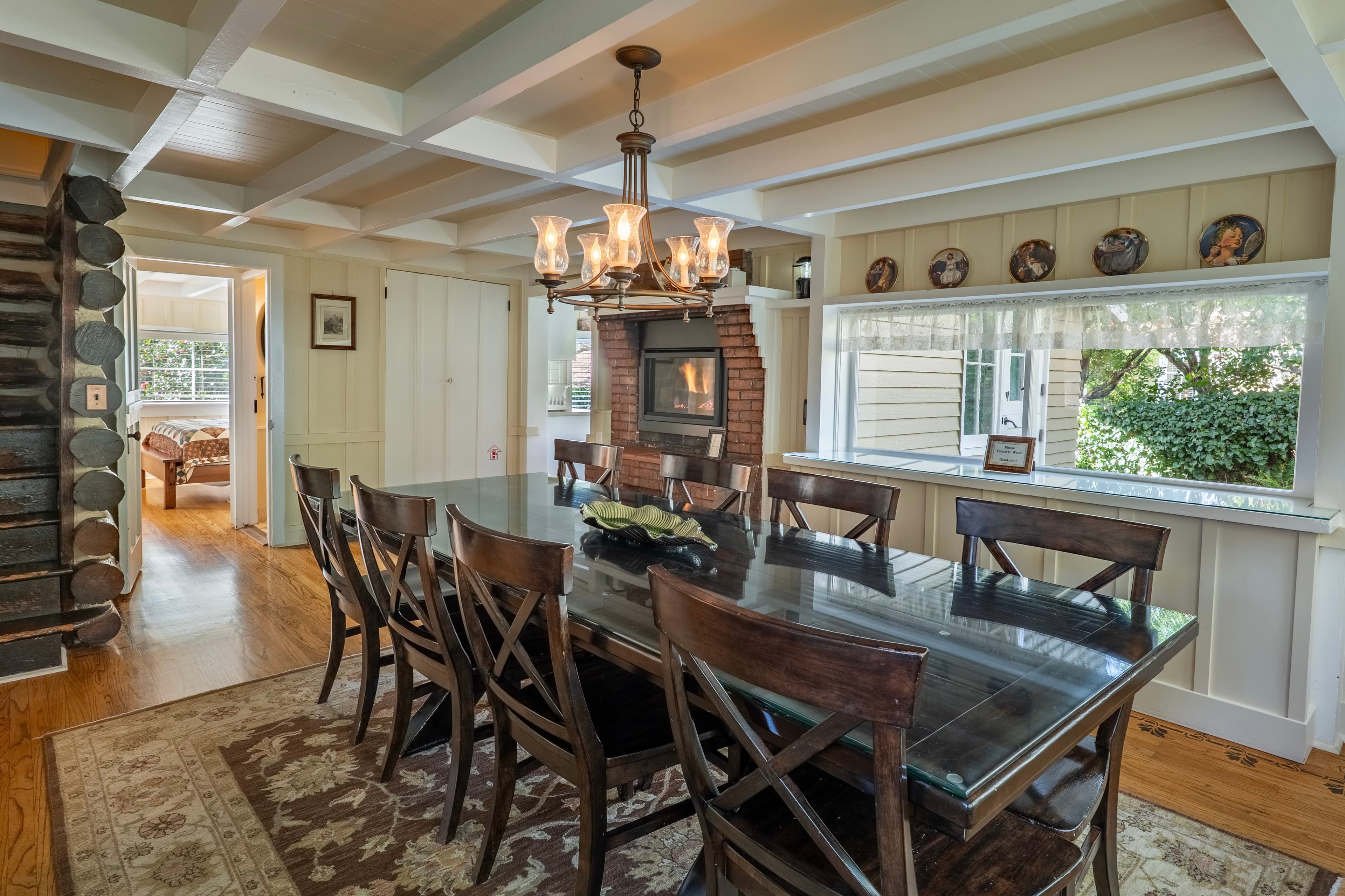 A cozy dining room with a large table, chandelier, and a view of a fireplace.