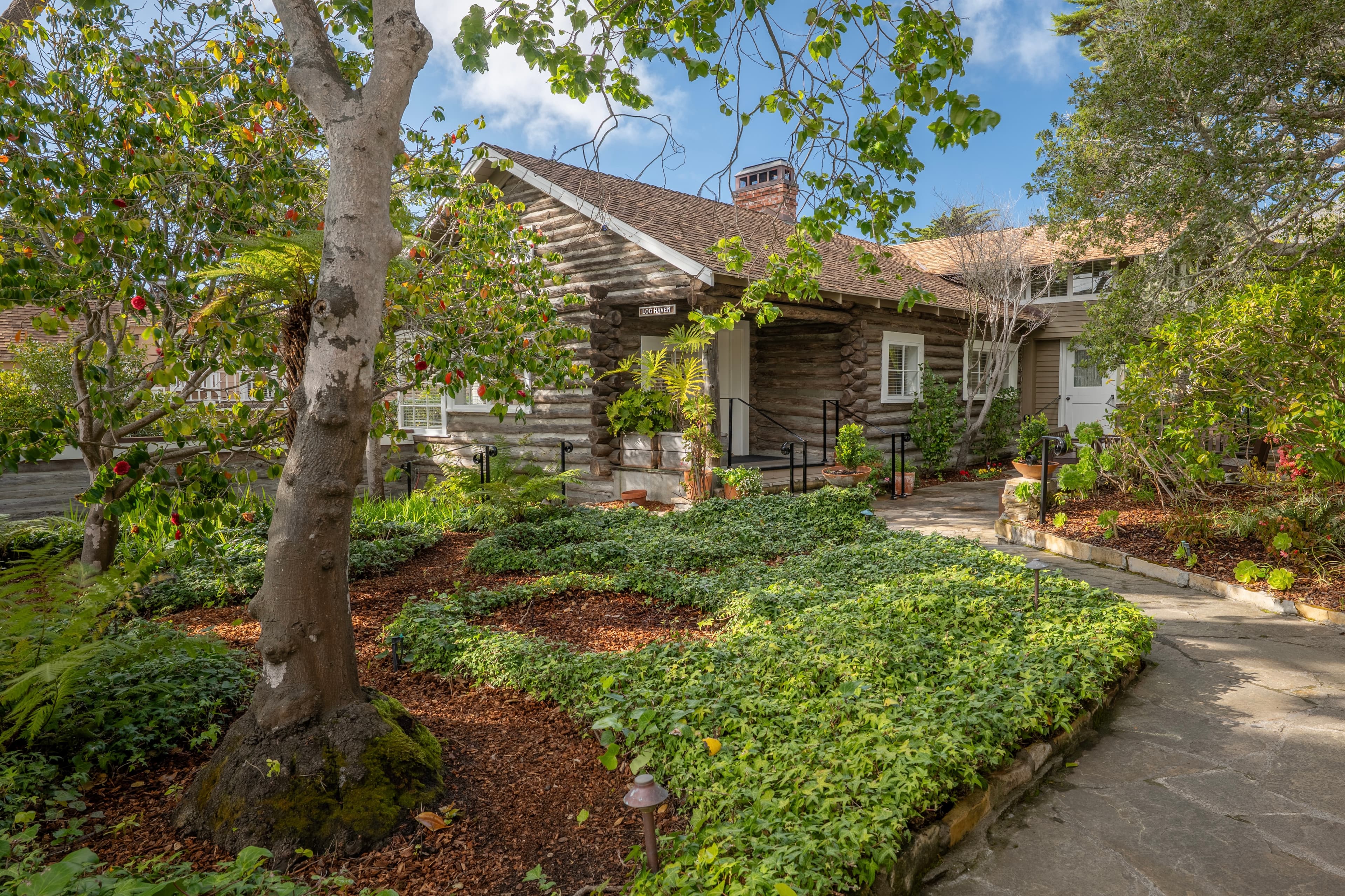 A charming log cabin surrounded by lush greenery and landscaped pathways.
