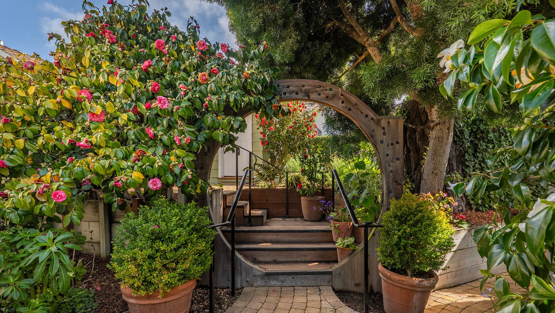 A charming garden pathway with lush greenery and vibrant flowers leading through an archway.