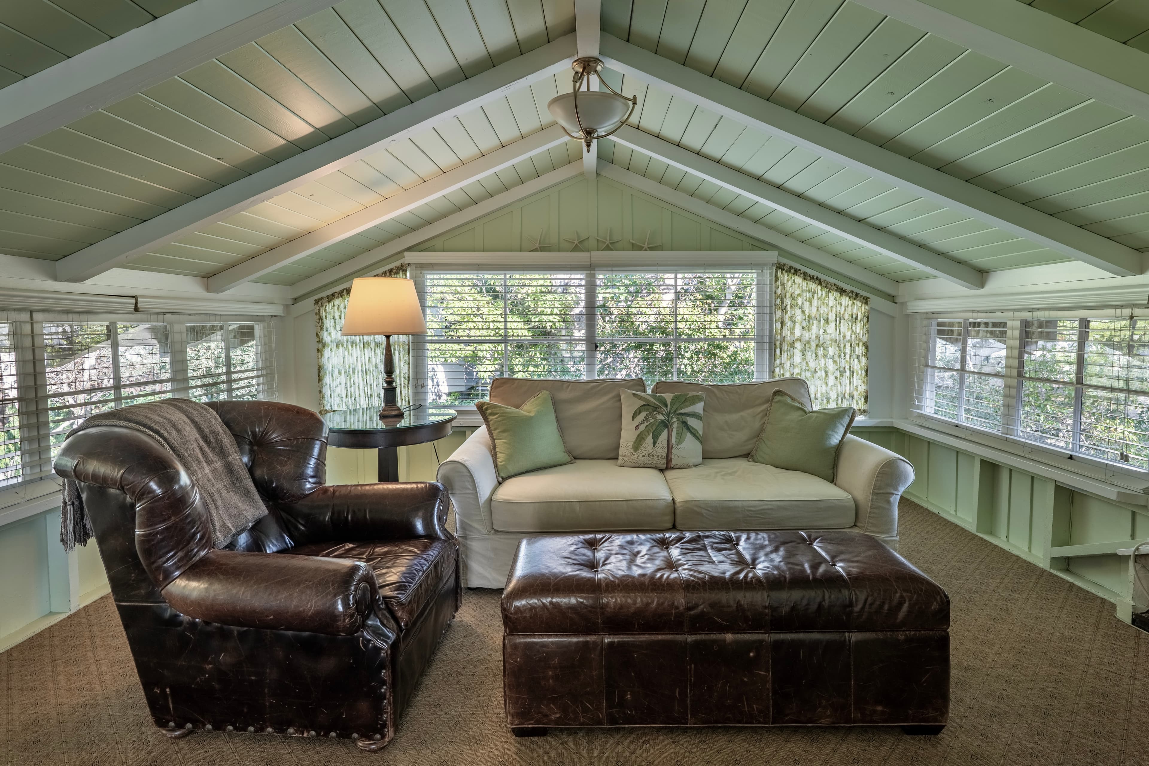 Cozy sitting area with a leather chair, light-colored sofa, and a coffee table under a sloped ceiling.