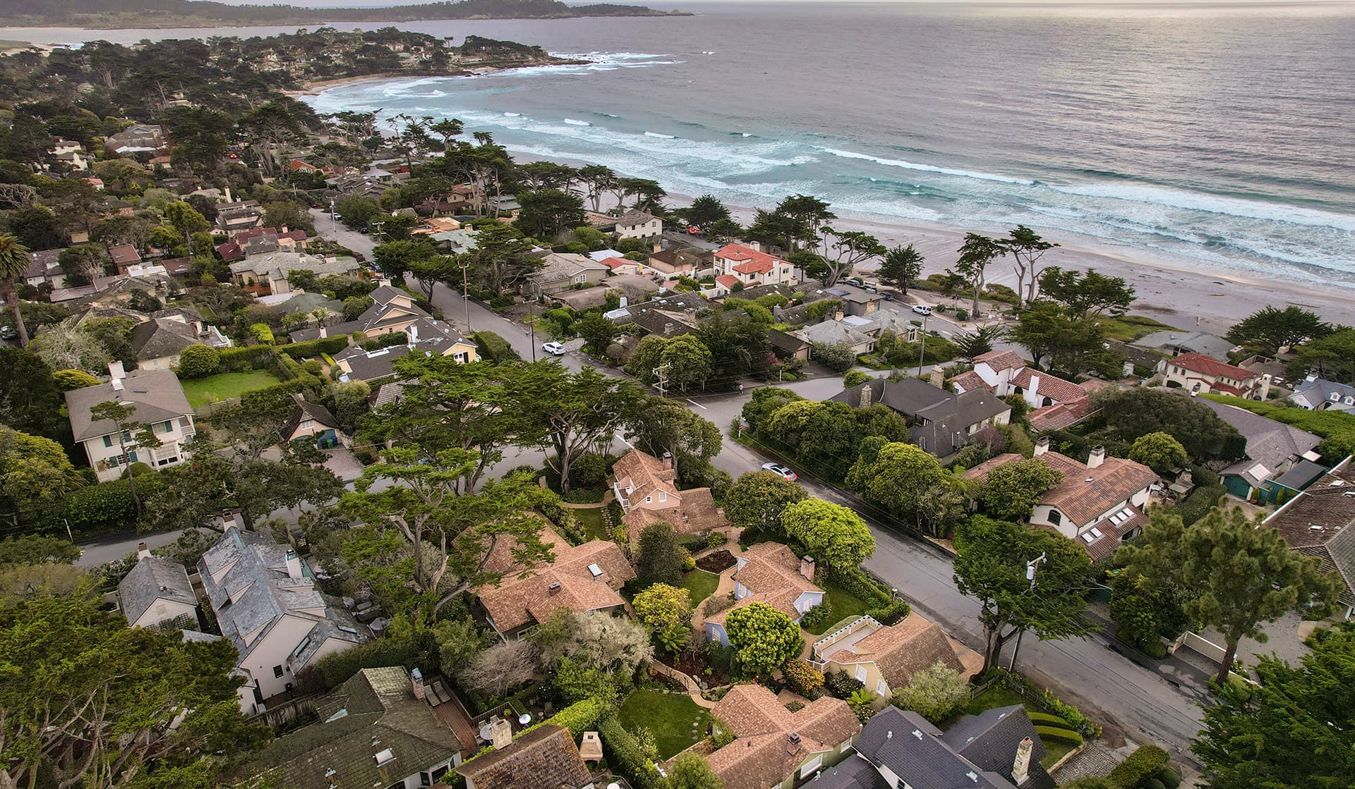 Aerial view of a coastal neighborhood with houses and waves in the background.