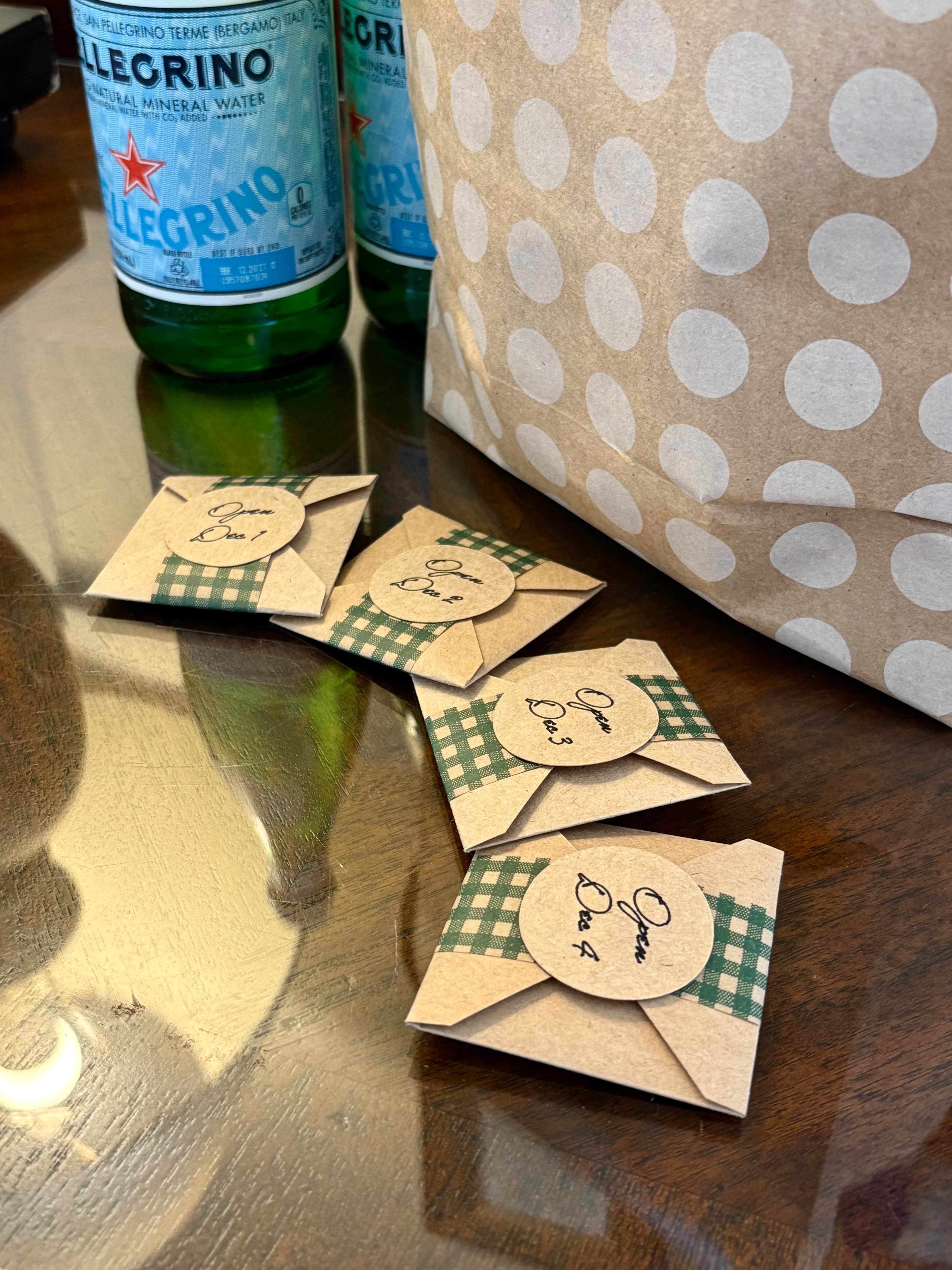 Four small, packaged items labeled with numbers are arranged on a table beside two bottles of sparkling water and a polka-dotted bag.