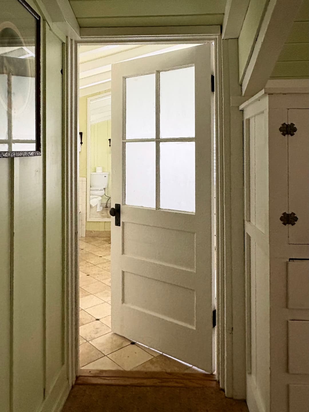 Third old door with a glass panel, there is a mirror inside the room reflecting a toilet.